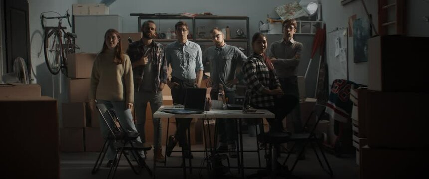 WIDE Small team of young entrepreneurs posing and looking into camera. Launching their small IT business startup company from garage. Shot with 2x anamorphic lens