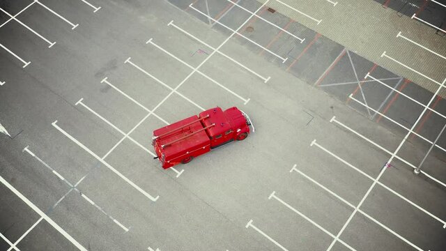 Vintage red vehicle, old fire engine equipped with tools for firefighting tasks, driving on empty parking. Aerial shot
