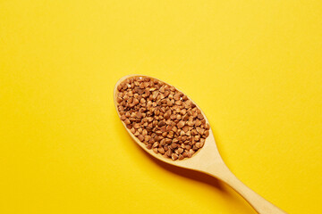 Top view of the wooden spoon filled with uncooked buckwheat isolated on the yellow background