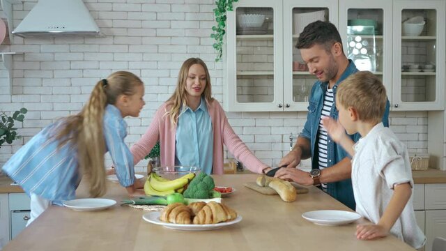 Smiling Father Cutting Baguette And Making Sandwiches For Kids In Kitchen