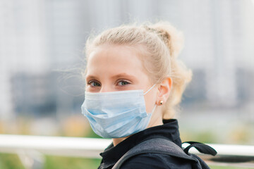 Schoolgirl in protective medical mask at sunset. Modern pupil with backpack during covid quarantine.