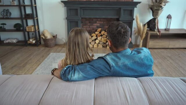 Back view of couple talking and hugging on couch at home