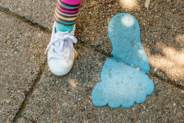 Little girl's foot next to big painted foot on sidewalk, big blue foot painted on the road,