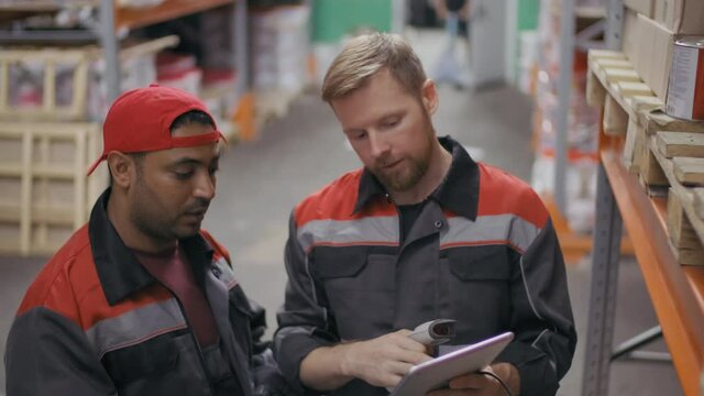 Medium footage of construction supervisor showing middle-eastern workman process of scanned barcodes on digital tablet standing among boxes at big warehouse