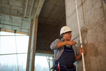 Wide angle portrait of female worker wearing hardhat and setting up pipes while working on...