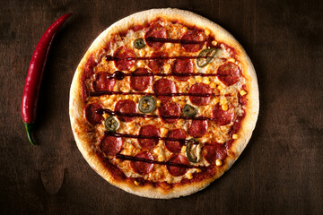 Spicy pepperoni pizza with corn and jalapeno pepper on a dark wooden background. Top view of a cooked barbecue pizza. banner