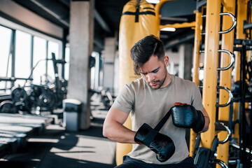 Young man preparing for exercising with boxing gloves in the gym.