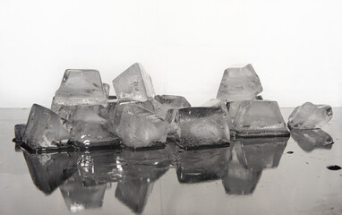 Ice cubes melting on dark reflective surface, white background, selective focus.