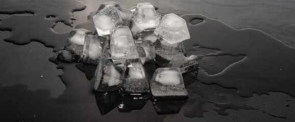 Ice cubes melting on dark reflective and illuminated surface, selective focus.