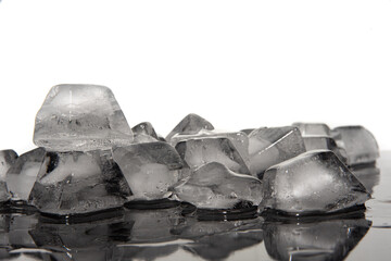 Ice cubes melting on dark reflective surface, white background, selective focus.