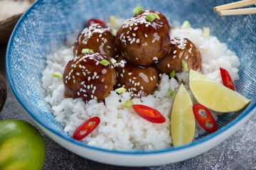 Close-up of white rice with fried pork meatballs in teriyaki sauce served in a blue bowl, selective focus