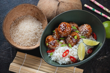 Chinese-style white rice with sweet sauce meatballs served in a green bowl, elevated view on a dark brown stone background