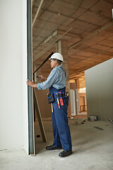 Vertical full length portrait of modern female worker holding screwdriver while building wall on construction site
