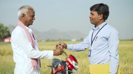 Farmer receiving keys from banker or corporate officer and doing handshake for two wheeler loan sanction - concept of business, bank loan and rural Indian lifestyle