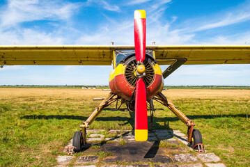 Small old yellow and red plane standing in summer field front view