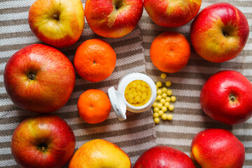 Red apples and tangerines lie around jars of vitamins on a mottled light canvas, focus on the fruit