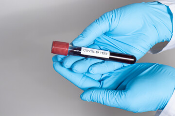 Hands in blue gloves hold a blood test for coronavirus. Diagnosis of the virus in the human body, mutations with pneumonia. With a place for text on a light gray background.