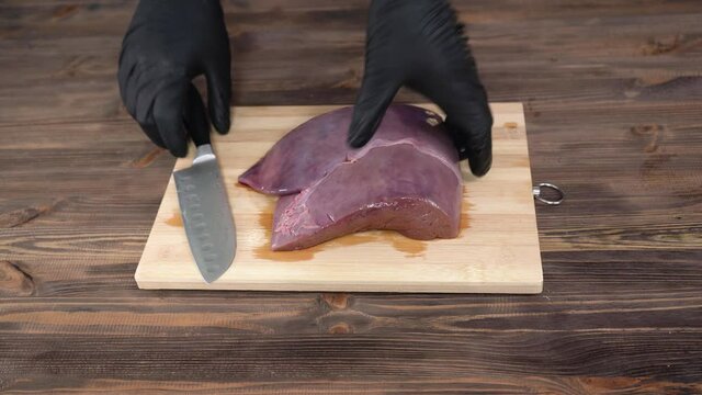 black-gloved chef removes film from beef liver