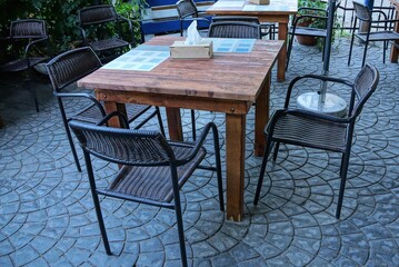 brown wooden table and black chairs stand on a gray sidewalk in the street of an outdoor restaurant