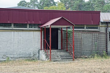 red canopy over porch with brown door and concrete threshold with steps on gray building outside