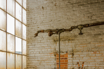 Old pipe running along painted brick wall next to frosted windows in an abandoned factory in the deep south
