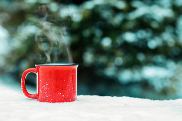 A red cup with a hot winter drink (mulled wine, cocoa, coffee, tea) against the background of a winter forest and snow. Winter mood and comfort.