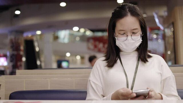Asian Business woman wear face mask to prevent Coronavirus. Use smartphone to find out about epidemic COVID-19. Social distancing in community or restaurant. Concept Health care new normal