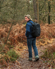 Man in jeans with backpack hiking on path in autumn forest.
