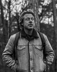 Man in jeans jacket with backpack in forest. Black and white photo.