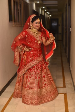 Young Indian Bride in her traditional wedding dress smiling and posing for photographs. She is not looking directly towards the camera