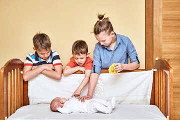 Happy elder brothers look carefully and touch gently lovely baby sibling wearing soft white body...