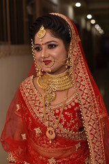 Young Indian Bride in her traditional wedding dress smiling and posing for photographs. She is traditional red color lehenga 
