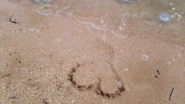 A woman draws a heart on the seashore which is washed away by a wave. The wave washes away the heart nestled in the sand. Woman draws a heart in the sand