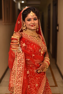 Young Indian Bride in her traditional wedding dress smiling and posing for photographs. She is not looking directly towards the camera