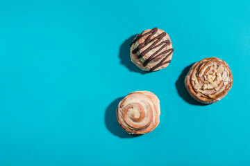 Three Cinnabon buns on a blue background with hard shadows.