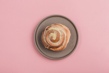A classic Cinnabon bun lies in a plate on a pink background.
