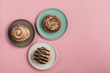 Three Cinnabon buns lie in plates on a pink background.