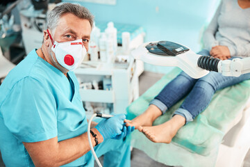 Professional specialist chiropodist in blue gloves looking at the photo camera in medical center