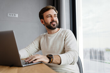 Handsome focused man working with laptop while sitting at table