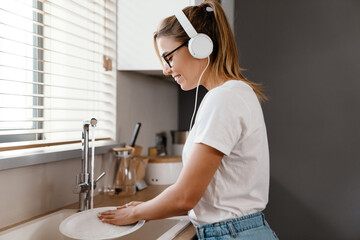 Beautiful cheerful girl in headphones smiling and washing dishes