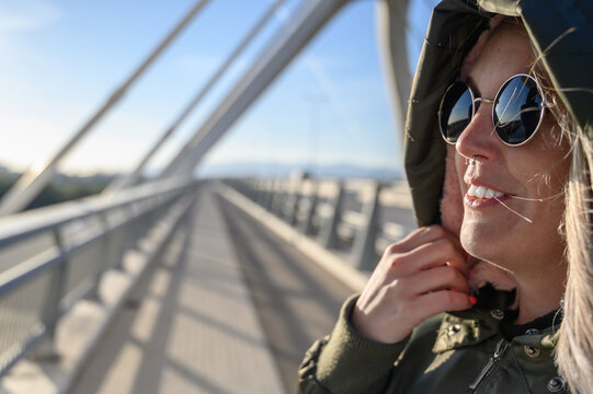 Mujer invierno exterior en puente con gorro capucha y gafas de sol sonriente y feliz