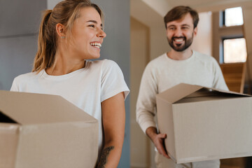Beautiful couple smiling and carrying cardboard boxes in new apartment