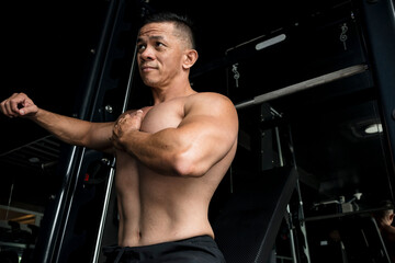 A fit Filipino male stretches and warms up his chest muscles in preparation for a bench press. Gym...