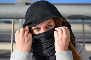 mujer blanca con un pañuelo tapando nariz y boca ojos verdes y capucha en exterior