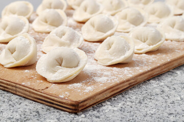Fototapeta na wymiar Raw ravioli (or dumplings) on wooden board on stone table, small depth of focus.