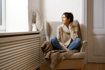 Fototapeta premium Smiling lady in smart trendy wear is sitting on armchair. Smiling, sitting in relaxing atmosphere indoors at home, nice design. Comfort and cozy girlish time