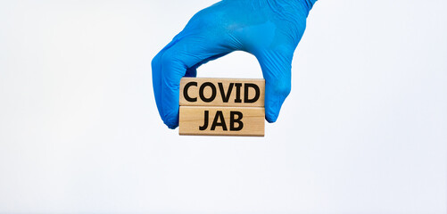 Covid jab symbol. Hand in blue glove holds wooden blocks with words 'Covid jab'. Beautiful white...