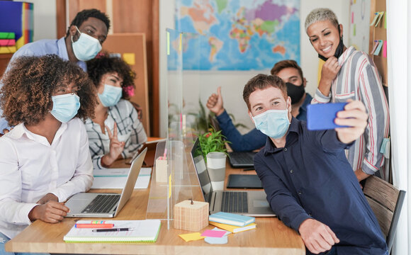 Multiracial people taking a selfie in coworking office while wearing protective face masks for coronavirus