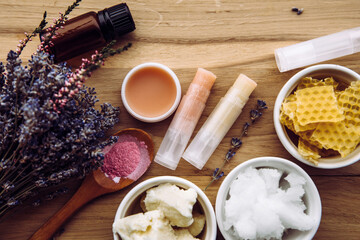 Ingredients for homemade lip balm: shea butter, essential oil, mineral color powder, beeswax, coconut oil. Homemade lip balm lipstick mixture with ingredients scattered around. - obrazy, fototapety, plakaty