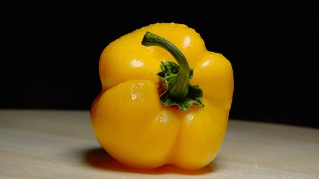 big yellow pepper with water drops on wooden board with black background